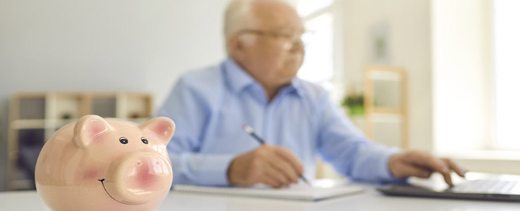 retired man looking over savings with piggy bank