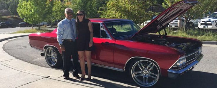 man and woman next to red muscle car