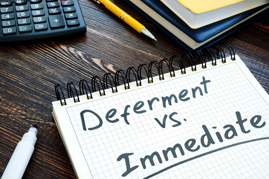 A spiral notebook with the words "Deferment vs. Immediate" written on its page