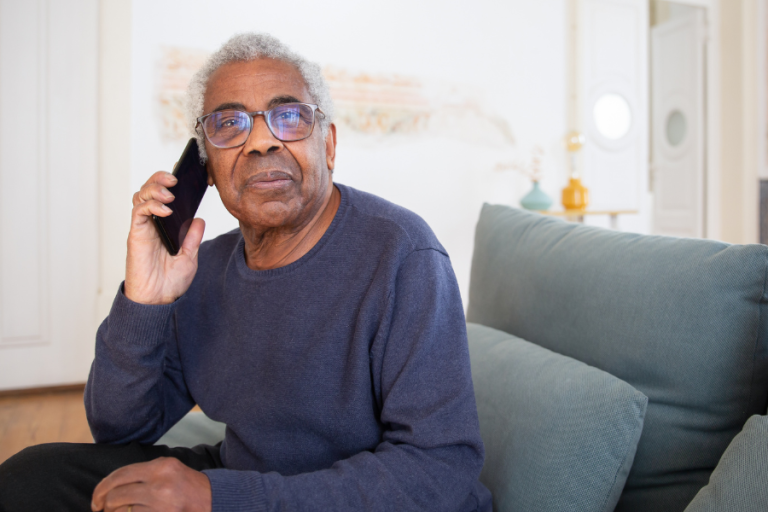 older black person holding a phone and looking at the camera while sitting on a couch